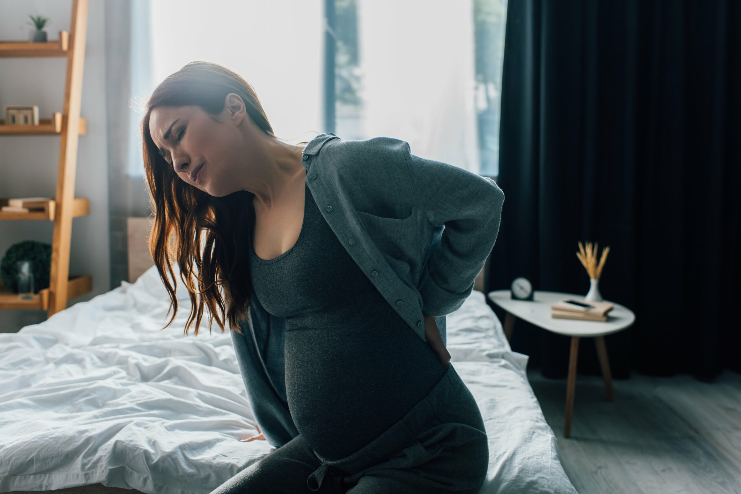 pregnant woman with back pain sitting on a bed