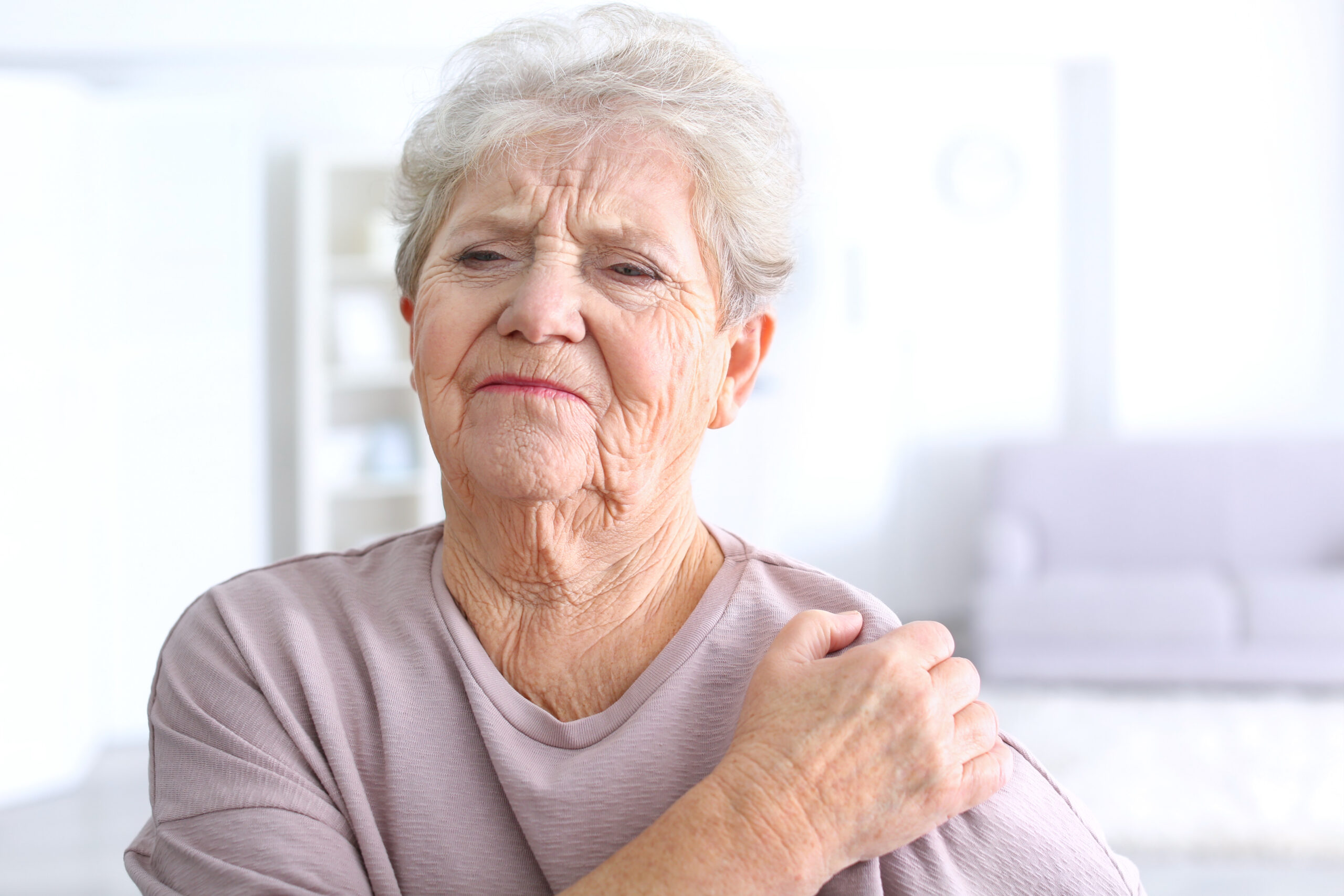 Elderly lady holding her shoulder due to chronic shoulder pain